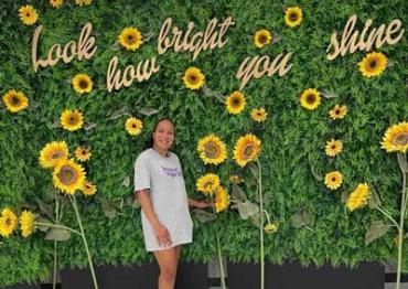 Saida standing in front of wall of sunflowers and words "look how bright you shine"