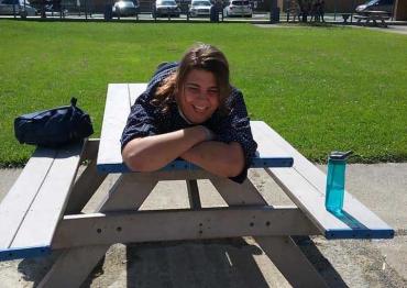 A woman smiling and laying across a picnic table in a park