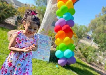 Valeria outside in front of a rainbow balloon arch