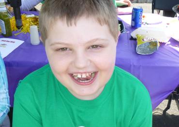 a little boy in a green shirt sitting at a picnic table and smiling