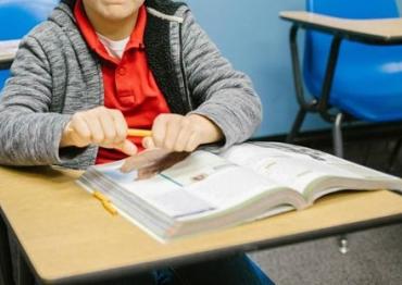 a frustrated child sitting at a desk trying to snap a pencil in half