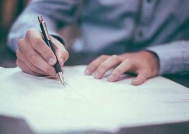 person in a blue button up shirt writing with a pen