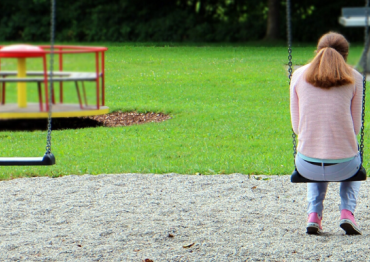 Girl sitting on a swing set alone in a park 