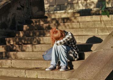 teenage girl sitting on steps outside with her head down in her lap