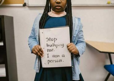 young girl holding a sign that says 'stop bullying me. I am a person'