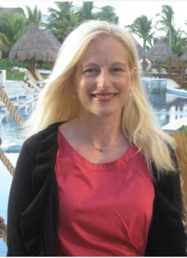 A women smiles in a red shirt and a black sweater at the camera 