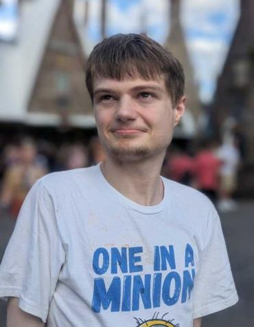 A young white man looks off in the distance, he wearing a white t-shirt that says "one in a minion" in blue font 