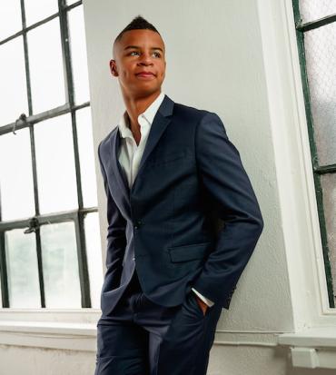 Armani Williams wearing a suit and leaning against the wall