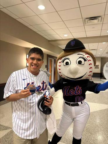 Dom wearing a Mets jersey standing with a Mets mascot