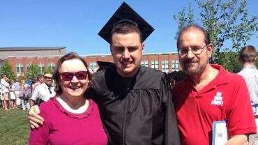 Ian H. wearing his cap and gown at graduation with his parents