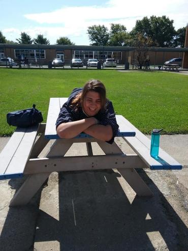 A woman smiling and laying across a picnic table in a park