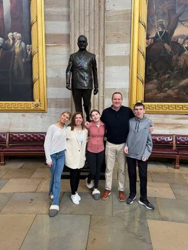 Senator Schmitt standing in congressional hallway with his wife, two daughters and son