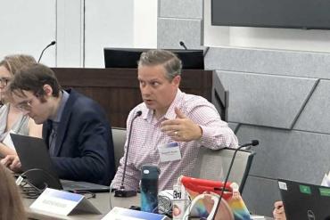 Tom Frazier sitting at conference table, speaking into microphone