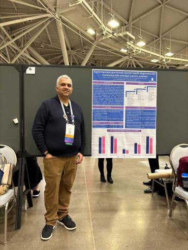 Vijay Vasudevan standing in front of a poster with his research