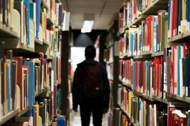 a student wearing a backpack and walking through an aisle of the school library