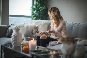 a woman with blonde hair on a couch with a small white dog