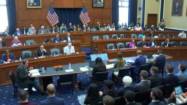 view of members of Congress seated in three rows in US Congressional hearing room