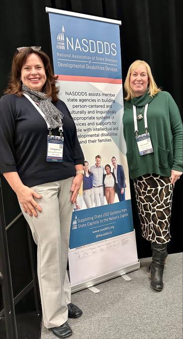 Christa Stevens and Kelly Headrick standing next to tall NASDDDS conference sign