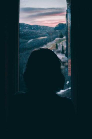 silhouette of a woman looking out the window on a stormy day