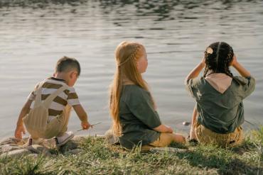 three children sitting near a lake