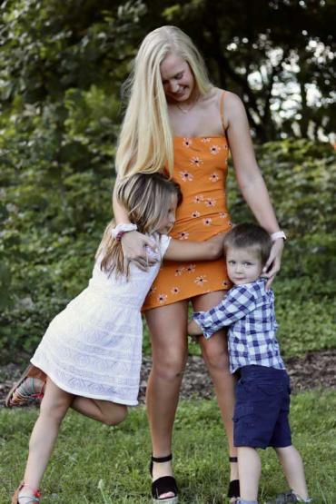 two children hugging the legs of a woman with blonde hair