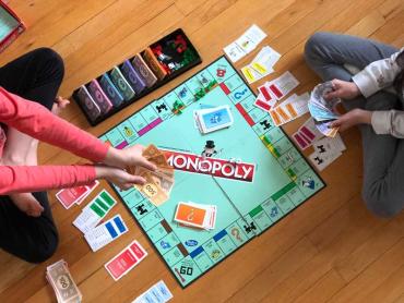 two children playing Monopoly on a wood floor