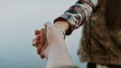 person in a flannel shirt and fur vest holding the hand of someone behind them